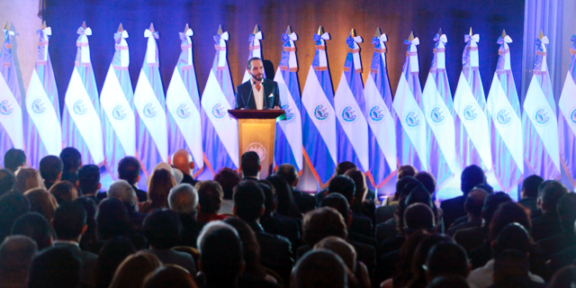 Najib Bukele presenting his government plan in front of a backdrop of Salvadoran flags