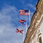The American flag flies over the flag of Puerto Rico on top of a colonial building